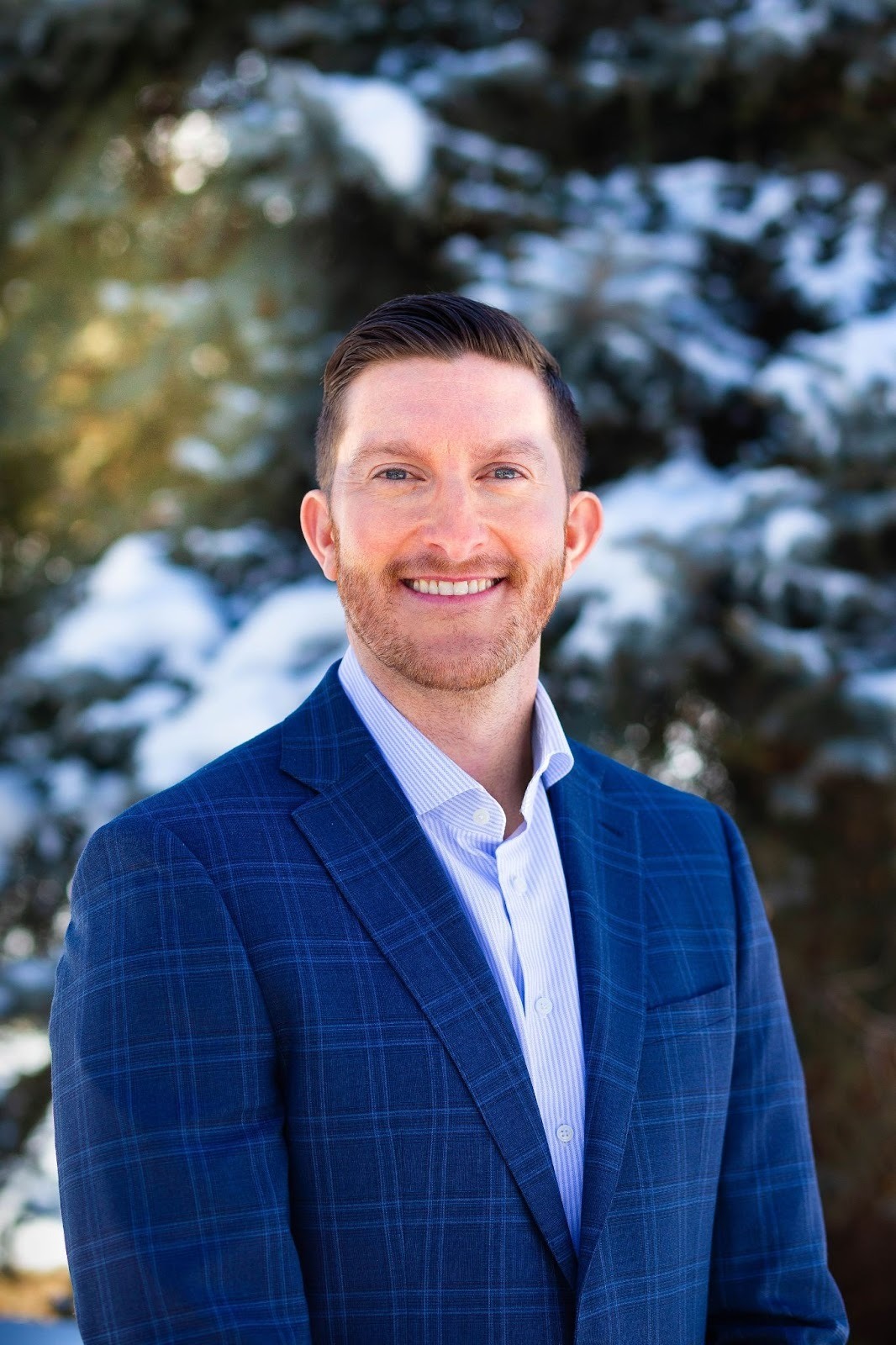 Dr. Matt Goergen, board-certified orthodontist at Southwest Pediatric Dentistry & Orthodontics, standing outdoors in a professional blue suit, with a blurred background of trees, representing orthodontics in Littleton, CO.