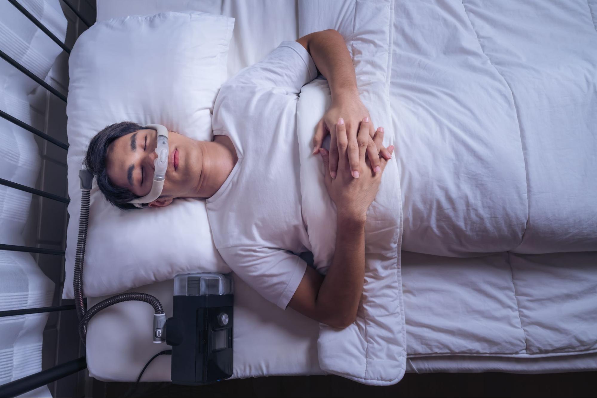 Young man sleeping with CPAP machine for sleep apnea treatment, emphasizing connection between orthodontics and improved breathing at Southwest Pediatric Dentistry & Orthodontics in Littleton.