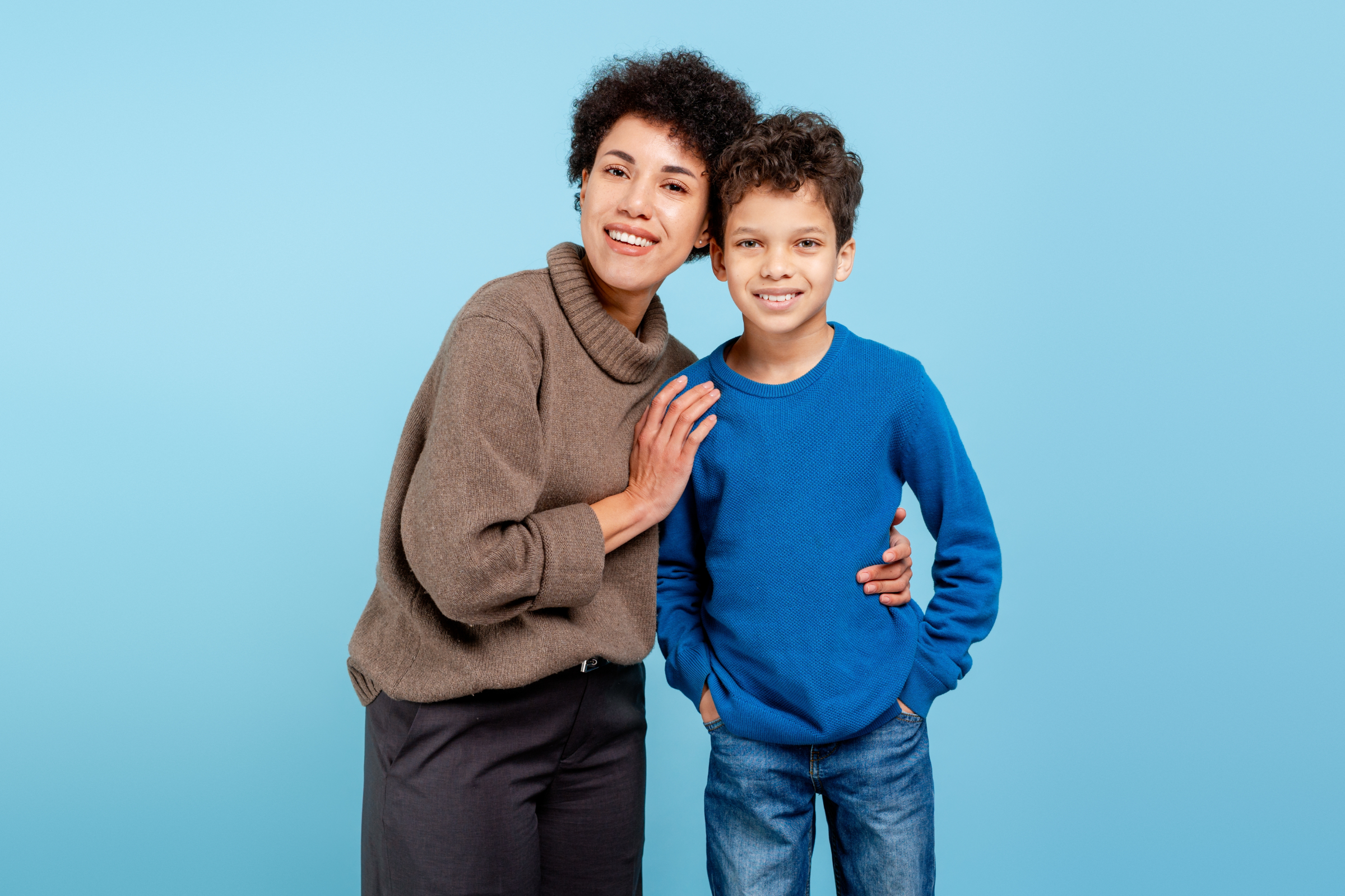 Smiling mother and son posing together against a light blue background, representing families choosing between a pediatric dentist and a family dentist at Southwest Pediatric Dentistry & Orthodontics in Littleton, CO.